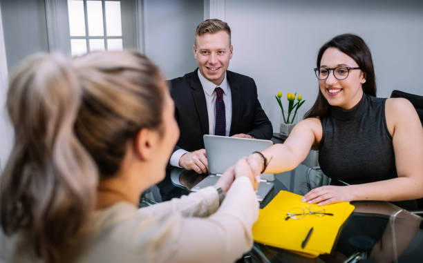 Group of young people in office environment, during the business meeting in the boardroom. Two women doing a handshake, man in the middle reacting cheerful.